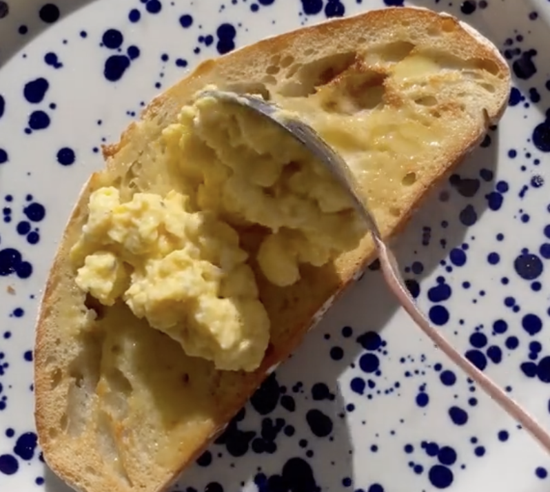 scrambled eggs being spread on sourdough bread slice
